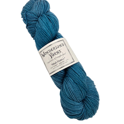 A skein of teal blue yarn with a white paper label reading 'Wonderland Yarns' and 'Mad Hatter', photographed on a plain light background.