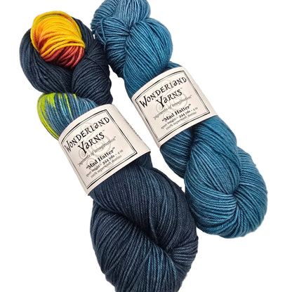 Two skeins of Wonderland Yarns Mad Hatter DeSTITCHnation yarn on a white background. One skein is a dark navy blue, and the other is a bright teal blue.