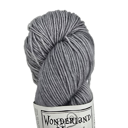 Close-up image of a single skein of Mad Hatter by Wonderland Merino Sport yarn in Tea Tray which is a light grey  color with label on a white background.