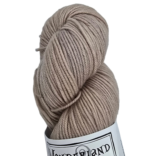 Close up image of a single skein of Mad Hatter by Wonderland Merino Sport yarn in Mushroom which is a light beige  color with label on a white background.