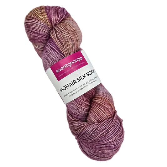 A skein of Sweet Georgia Mohair Silk Sock yarn in a variegated dusty purple, mauve, and rose gold colorway, with its paper label visible in the center, set against a plain white background.