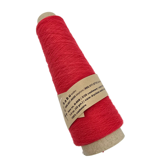 A cone spool of bright red yarn with a tan paper label, photographed diagonally on a plain white background.