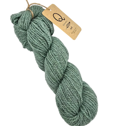 Image of a single skein of Owl by Quince & Co.yarn in the color Acacia a dusty sage green yarn with a kraft paper tag attached, photographed on a clean white background.