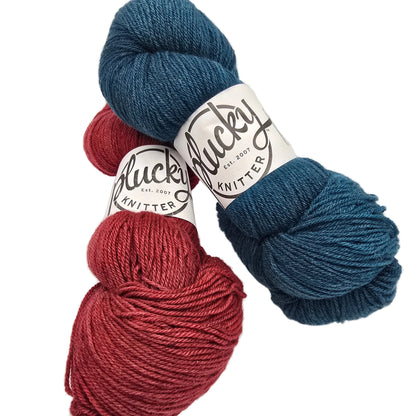 Image of two skeins of oxford Yarn by 
Plucky Knitters one in blue and one in a red with labels on a white background.