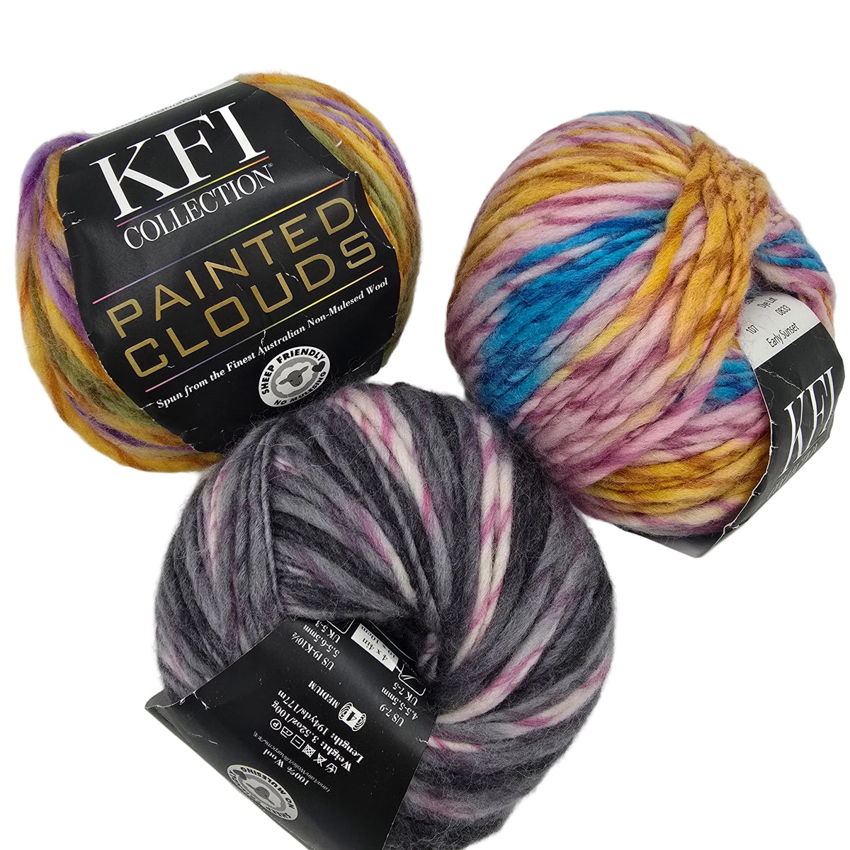 Three balls of KFI Collection 'Painted Clouds' yarn displayed on a white background, showing their black paper labels and the variegated yarn colors.