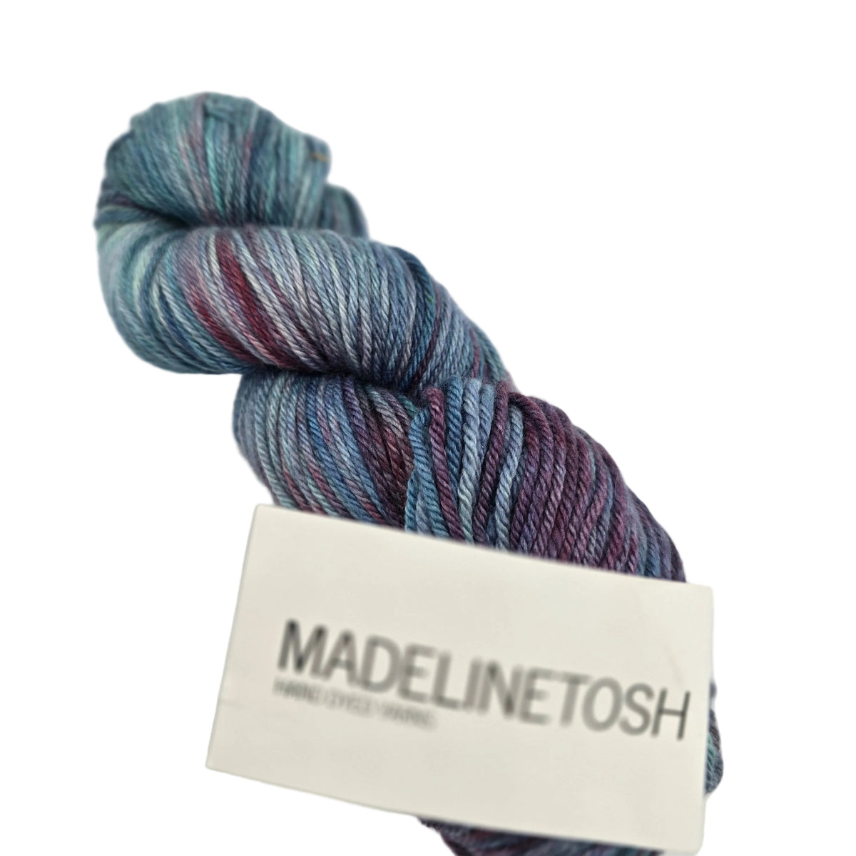 A single skein of Pashmina Worsted yarn by Madelinetosh  in the color Minnesota Winter sunset a variegated yarn with blue, teal, and purple/pink tones, featuring a white paper label printed with the brand name 'MADELINETOSH'.