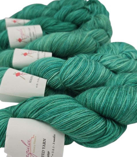 Image of multiple skeins of Peacock Green Luster by Anzula yarn with labels on a white background.