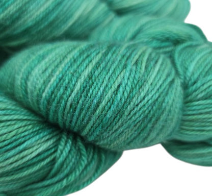 Close-up image of Luster by Anzula Yarn in the Color Peacock green on a white background.