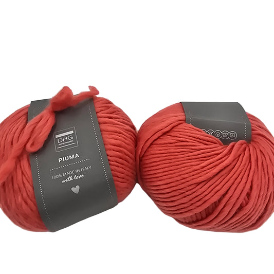Image of two balls of Piuma by DHG Ultra Soft bulky Italian Merino Wool  yarn in the color Coral which is a solid reddish orange with labels on a white background