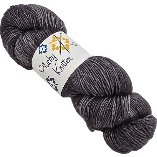 Image of a single skein of Plucky Knitter  Merino, Cashmere, Nylon blend yarn in the color Medieval which is a mid-grey with label on a white background.