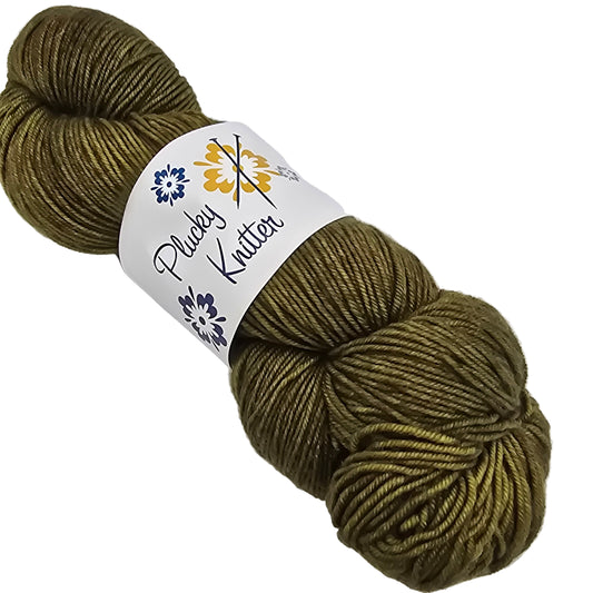 Image of a single skein of Plucky Knitter  Merino, Cashmere, Nylon blend yarn in the color Faded Grandeur which is a deep forest green with label on a white background.