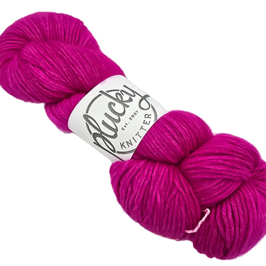 Image of Plucky Knitter cashmere yarn skein in the color Hotsy Totsy which is a bright pink with label on a white background.