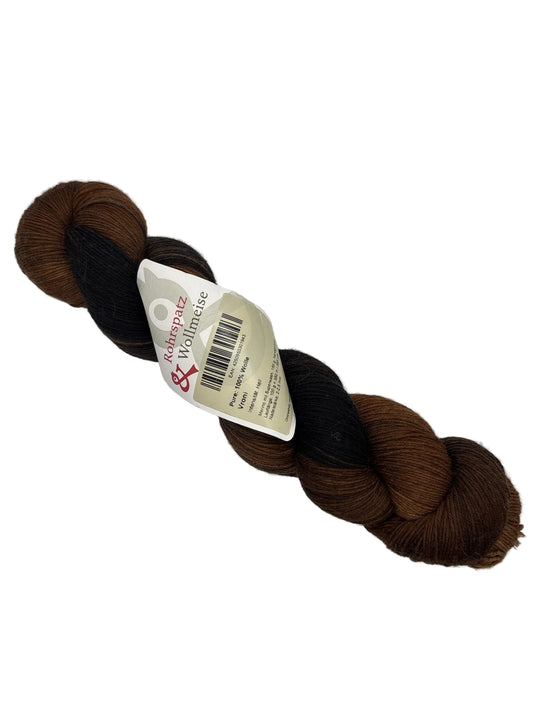 Image of a single skein of Pure: Vroni Yarn by Rohrspatz & Wollmeise in the color Hell (brown and Black) with label on a white background.
