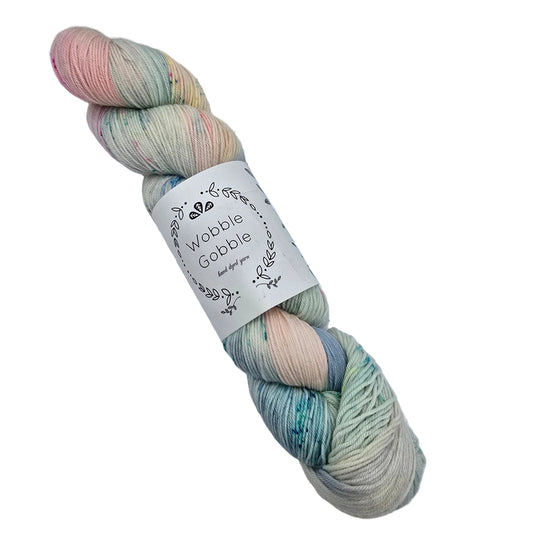 A single skein of variegated yarn with a white paper label reading 'Wobble Gobble hand dyed yarn' on a white background. The yarn features blended pastel shades of pink, mint green, blue, and cream.