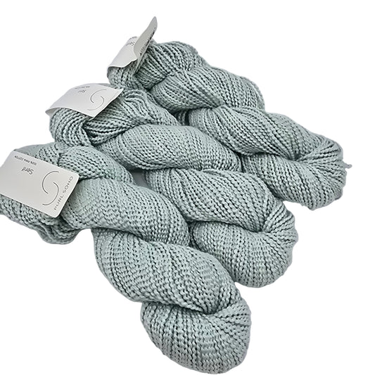 Image of three skeins of Serif by Purl Soho yarn in the color turquoise tint which is a pale blue with labels on a white background.
