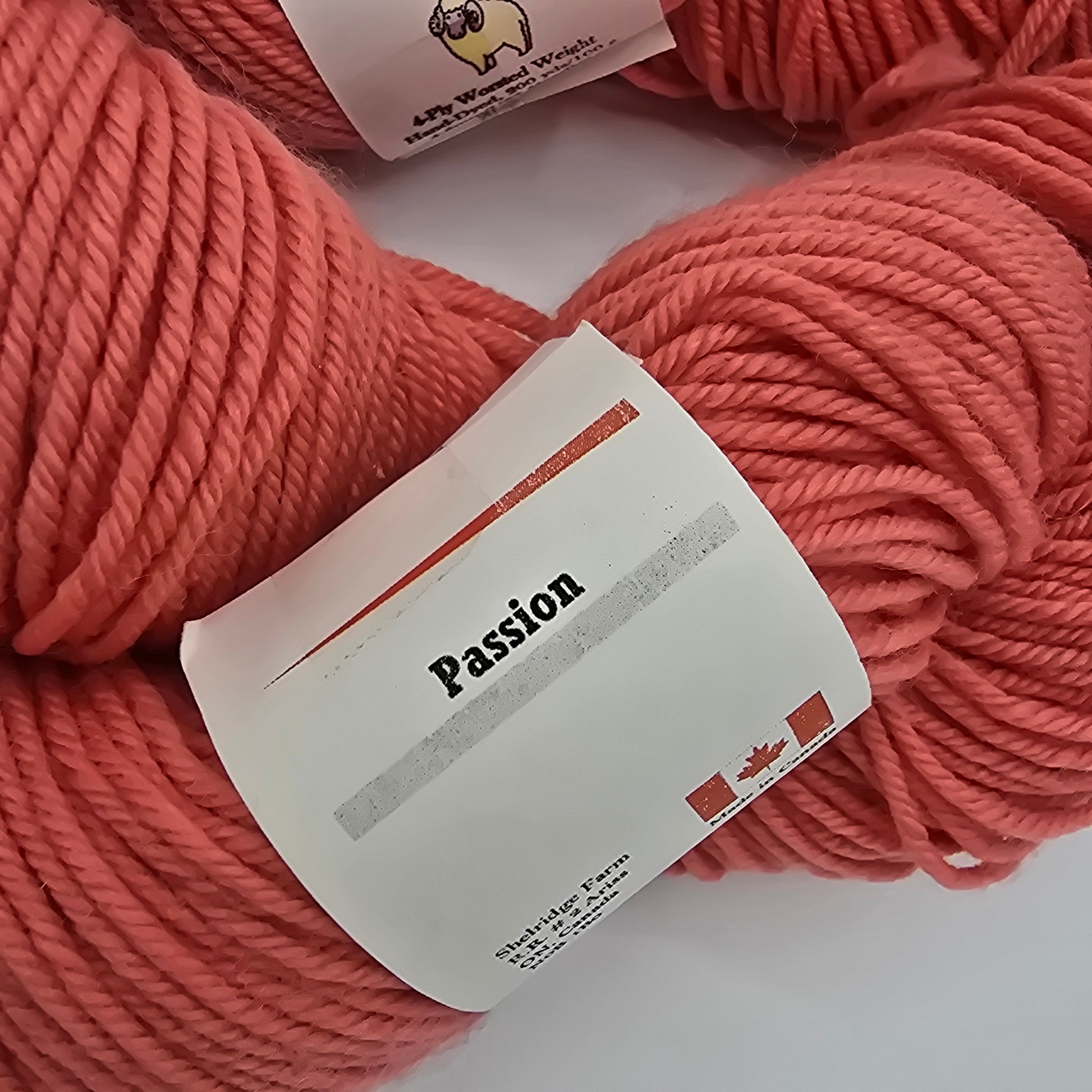 Close-up image of the label on a skein a Shelridge farm brand yarn in the color passion which is a coral pink on a white background.