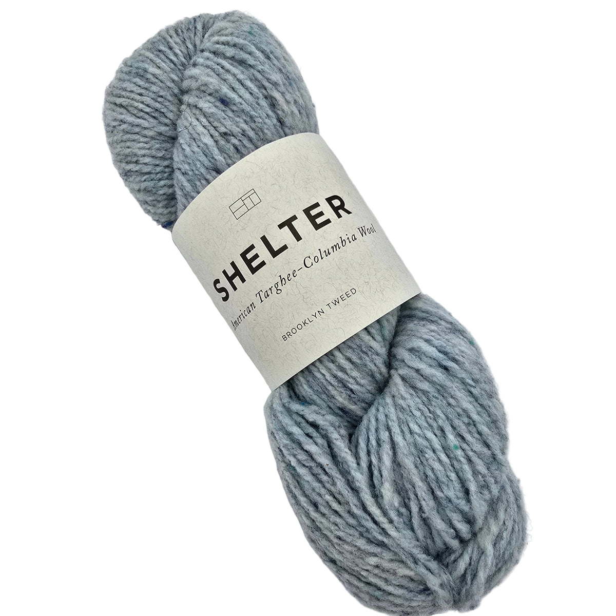 A skein of Shelter_yarn_by_Brooklyn_Tweed_in the color_Iceberg a dusty light blue-gray color, wrapped with a cream paper label on a white background.