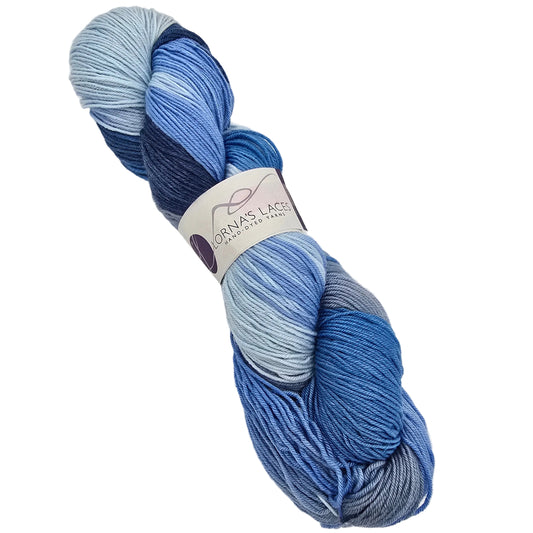 A skein of Shepherd_Sock_Multi_Yarn by_Lorna_s_Laces in the color a Lake_House variegated yarn from, featuring a color-shifting gradient of light blue, medium blue, navy, and gray, with a white paper label in the center on a white background.