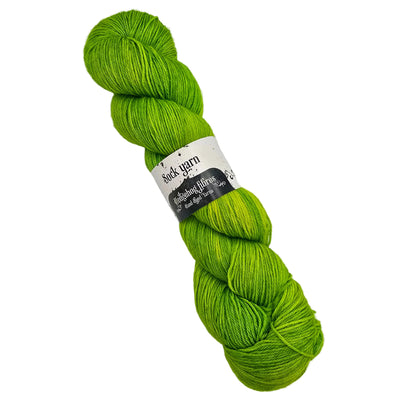 A single skein of Sock_Yarn_by_Hedgehog_Fibres_in the color_Shamrock a solid  green yarn  wrapped with a paper label on a white background.