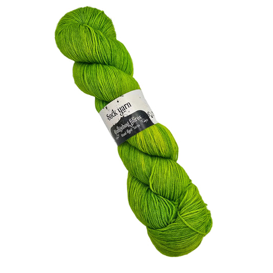 A single skein of Sock_Yarn_by_Hedgehog_Fibres_in the color_Shamrock a solid  green yarn  wrapped with a paper label on a white background.