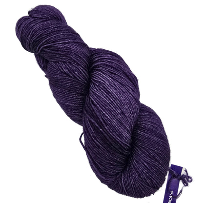 A skein of deep purple sock by malabrigo yarn in color 808 Violeta Africana with a subtle sheen, shown on a plain white background with a small purple product tag attached.