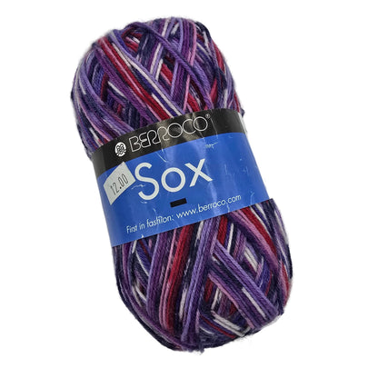 A skein of Berroco Sox yarn in a variegated purple, red, and white colorway, wrapped with a blue and black paper label.