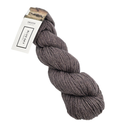 A skein of Sweater Worsted Yarn by Blue Sky Fibers in the color Grape Stomp a dusty purplish brown green yarn with a paper label attached, photographed on a clean white background.
