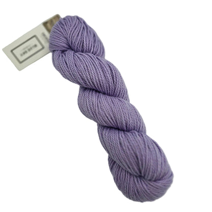 A skein of Sweater Worsted Yarn by Blue Sky Fibers in the color Lilac a light purple yarn with a paper label attached, photographed on a clean white background.