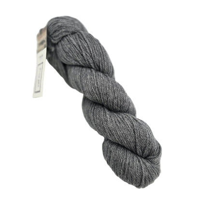 A skein of Sweater Worsted Yarn by Blue Sky Fibers in the color Manatee a light grey yarn with a paper label attached, photographed on a clean white background.