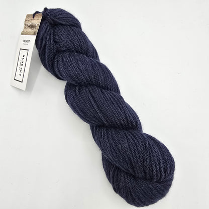 A skein of Sweater Worsted Yarn by Blue Sky Fibers in the color Rainstorm a Navy blue yarn with a paper label attached, photographed on a clean white background.