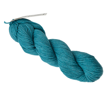A skein of Sweater Worsted Yarn by Blue Sky Fibers in the color waterslide a medium turquoise  yarn with a paper label attached, photographed on a clean white background.