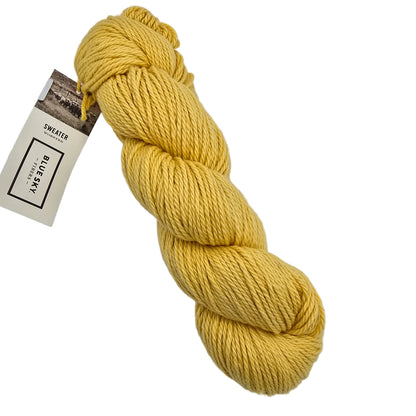 A skein of Sweater Worsted Yarn by Blue Sky Fibers in the color Firefly a Yellow yarn with a paper label attached, photographed on a clean white background.
