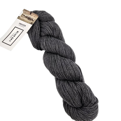 A skein of Sweater Worsted Yarn by Blue Sky Fibers in the color Grey Duck a dark grey yarn with a paper label attached, photographed on a clean white background.