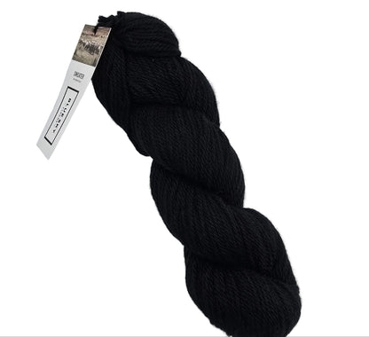 A skein of Sweater Worsted Yarn by Blue Sky Fibers in the color Penguin a black yarn with a paper label attached, photographed on a clean white background.