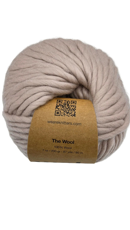 A skein of The_Wool_Yarn_by_We_Are_Knitters
a super chunky yarn in a soft dusty Beige color, wrapped with a brown paper label that reads 'The Wool' and 'wearknitters.com'.