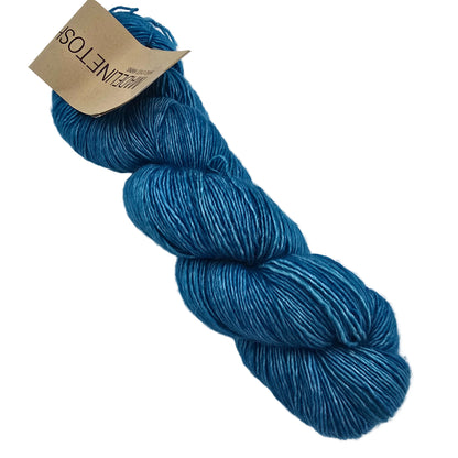 A skein of Tosh_Merino_Light_Yarn_by_Madelinetosh_in the color_Plunge ateal blue yarn with a brown paper label on a white background.
