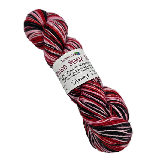 Image of a single skein of Vesper Sock Yarn by Knitterly Things in the color  Strange Little Mama with label on a white background.