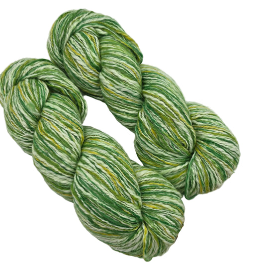 Image of two hanks of Winqu Alqa yarn by Mirasol Yarn in Color 1009 on a white background.