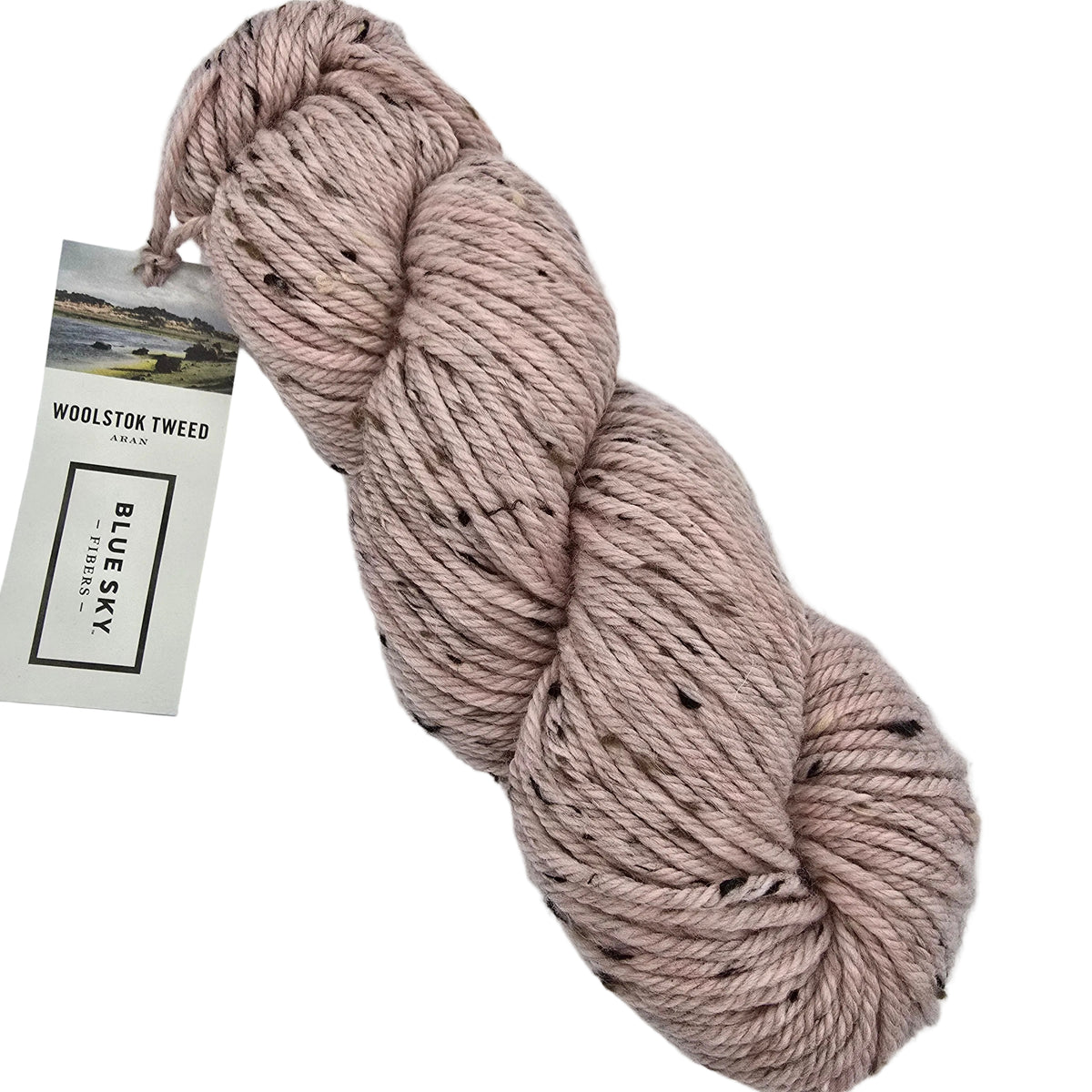 A hank Woolstok_Tweed_Yarn_by_Blue_Sky_Fibers in color 3301_Cactus_Flower a dusty pink wool yarn with black and white flecks, shown next to its paper brand tag on a 