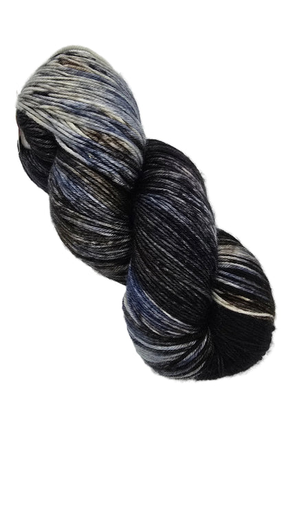 A single skein of Yowza_Yarn by_Ms._Babs_in the color_Suit_and_Tie a variegated yarn with blended black, navy, gray, and white tones, photographed on a plain white background.