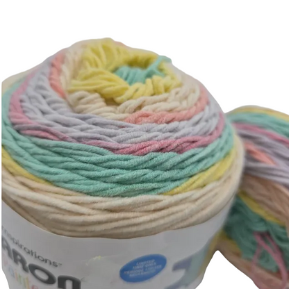 Close-up image of Caron Cotton Painterly Cakes Yarn in the color  Coral Cascade with partial label on a white background.