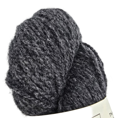 A close-up of a dark heather gray skein of yarn with a cream-colored paper label partially visible at the bottom, set against a plain white background.