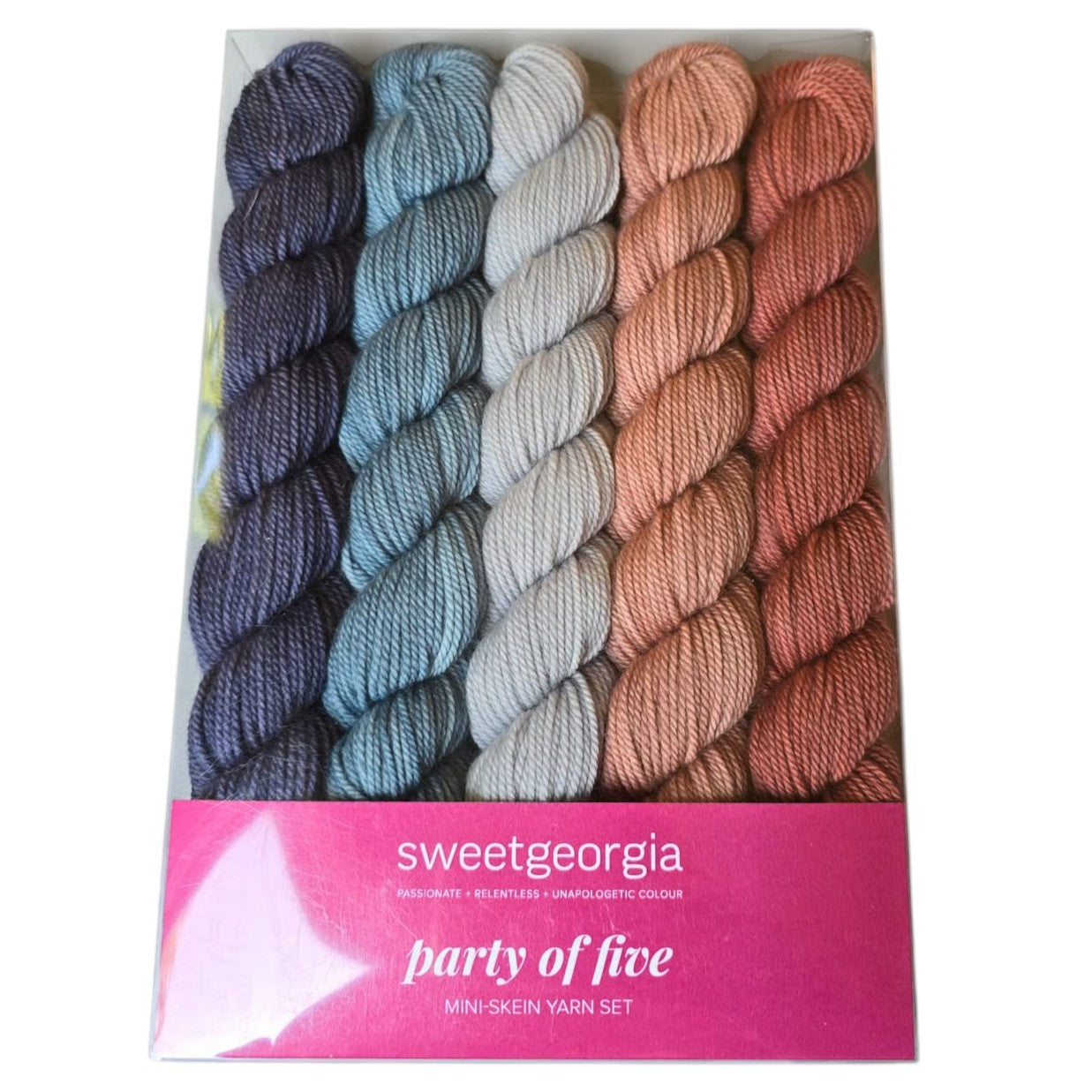 Image of a Sweetgeorgia brand  pack of 5 different colored mini skeins of yarn.  Colors include blue, grey and orange skeins. Color is called desert by the manufacturer, in a pink and white package with label on a white background.